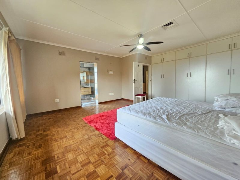 Spacious bedroom featuring classic parquet flooring, extensive built-in cabinetry, a ceiling fan, and direct access to an en-suite bathroom.