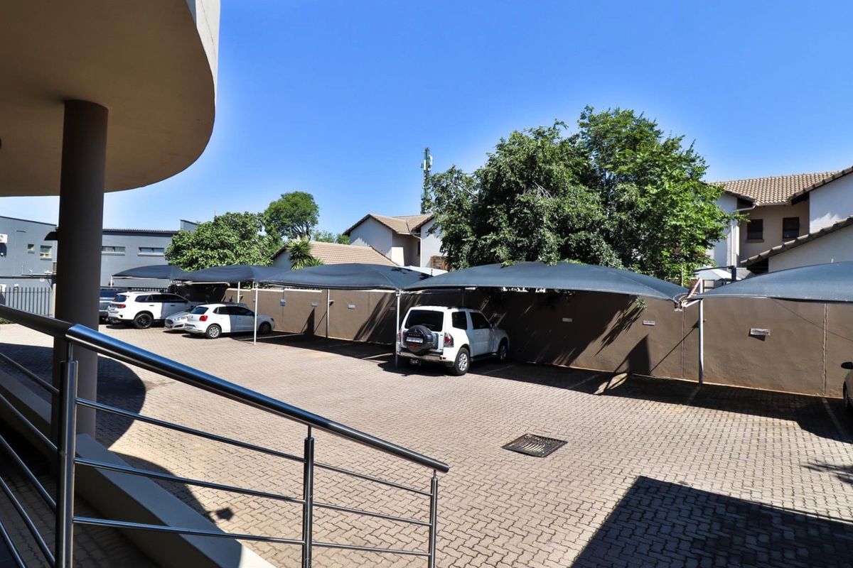 Commercial parking area featuring paved driveway, multiple shade cloth carports, and a stainless steel balustrade leading to the building entrance.