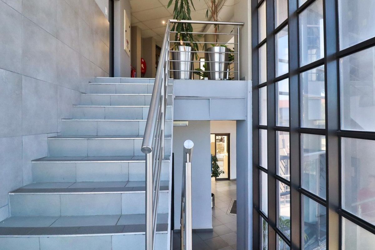 Modern commercial entrance featuring a tiled staircase with stainless steel balustrades and a large floor-to-ceiling grid-pattern window providing ample natural light.