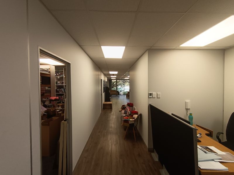 A functional office hallway featuring laminate flooring, suspended ceiling tiles, and recessed lighting, providing access to adjacent office spaces.