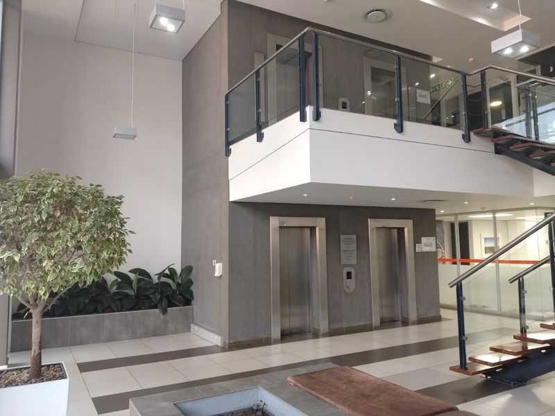 Modern office building lobby featuring dual elevators, a glass-railed staircase, and high-quality tiled flooring in a bright, professional setting.