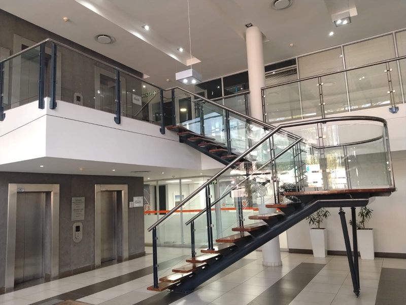 Modern office building entrance lobby featuring a prominent open staircase with glass balustrades, elevator access, and high-quality tiled flooring.