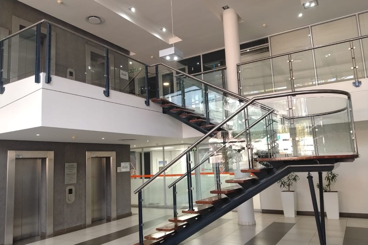 Modern office building entrance lobby featuring a prominent open staircase with glass balustrades, elevator access, and high-quality tiled flooring.