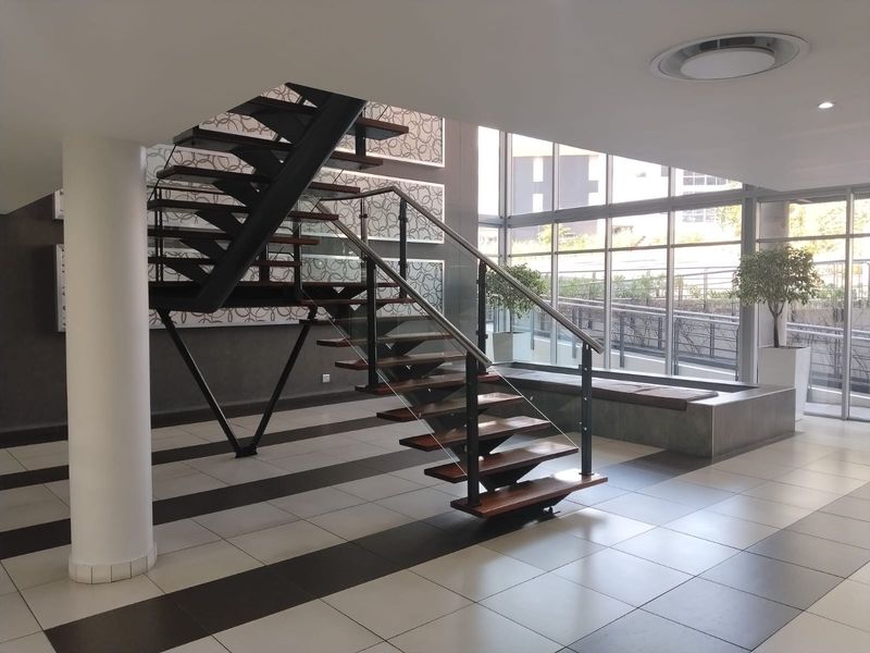 Modern office entrance featuring a striking open-tread staircase with glass balustrades, large floor-to-ceiling windows, and high-quality tiled flooring.
