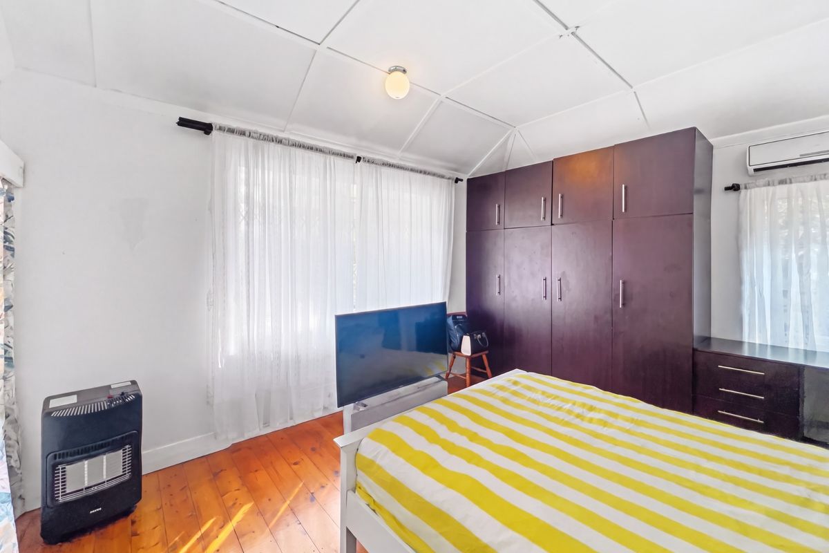 A bedroom featuring timber flooring, built-in dark wood cabinetry, and a wall-mounted air conditioning unit.
