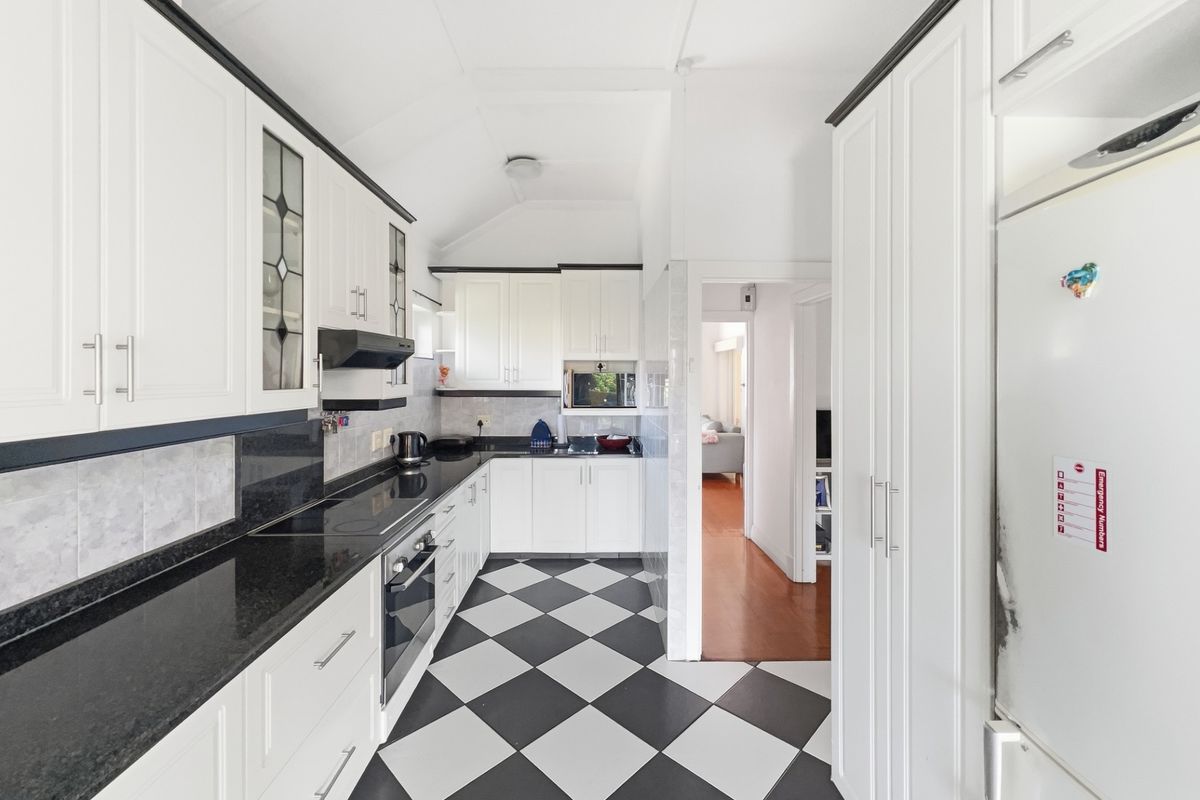 A well-maintained kitchen featuring white cabinetry, black granite countertops, a built-in oven, and a classic black and white checkered tile floor.
