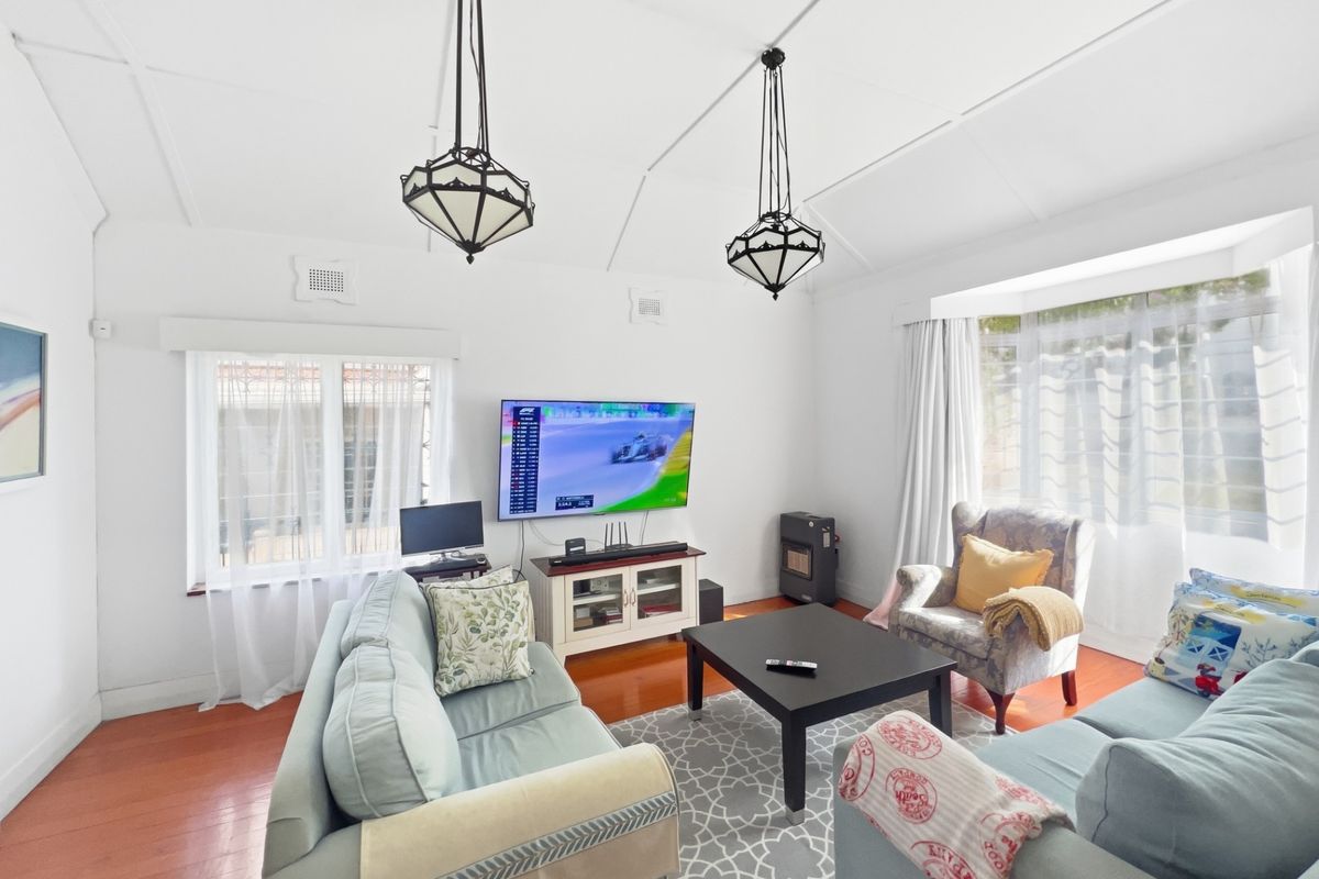 A bright and airy living room featuring polished hardwood floors, a vaulted ceiling with decorative pendant lights, and a built-in gas heater.