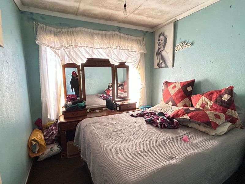 A bedroom featuring a window with curtains and a ceiling light fixture, currently showing significant signs of wear and required maintenance on walls and ceiling.