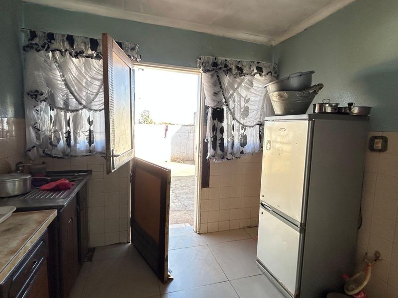 A dated kitchen featuring tiled splashbacks, basic cabinetry, and direct access to the exterior through a rear door.