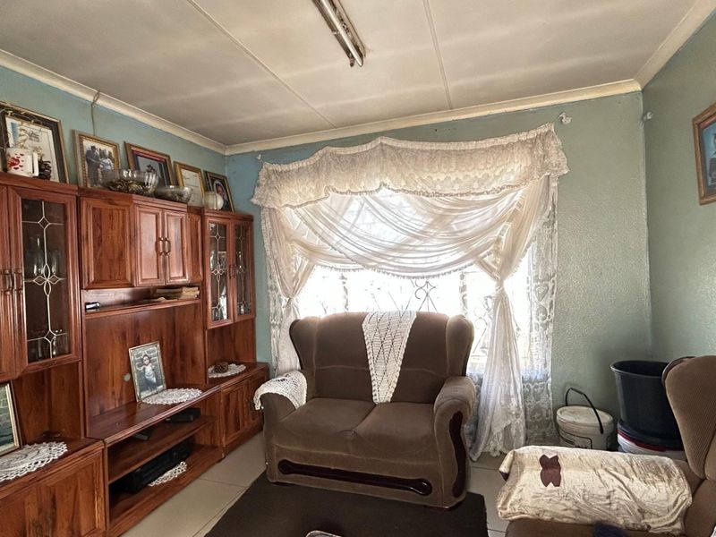 A living room featuring tiled flooring and security bars on the window, currently showing signs of wear on the ceiling and walls.