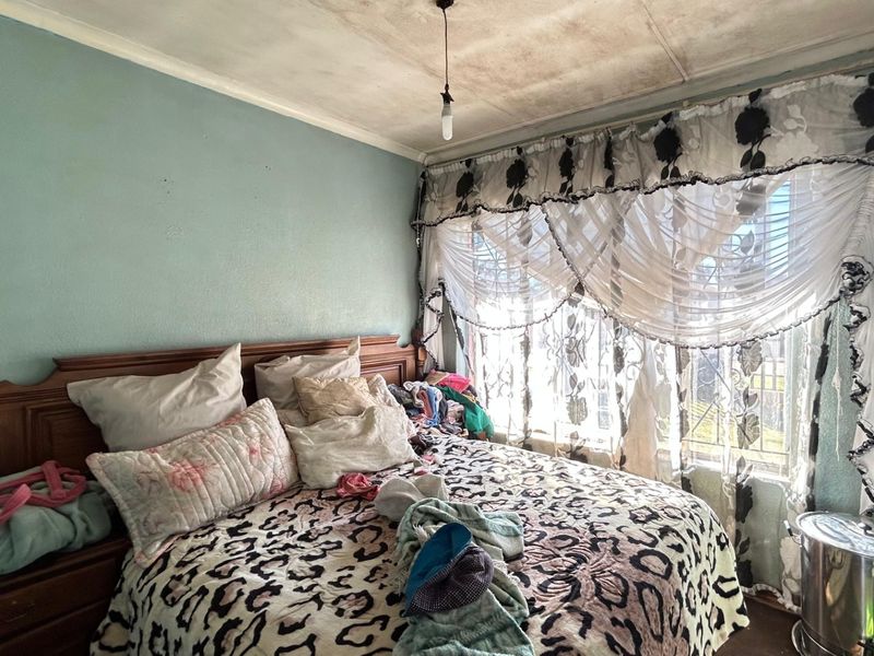 A bedroom featuring security bars on the window and visible ceiling water damage, requiring maintenance and cosmetic updates to improve the space.