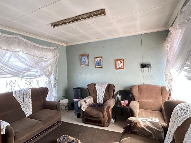 A living room featuring tiled flooring and security bars on the windows, currently showing signs of wear including ceiling damage and peeling paint.