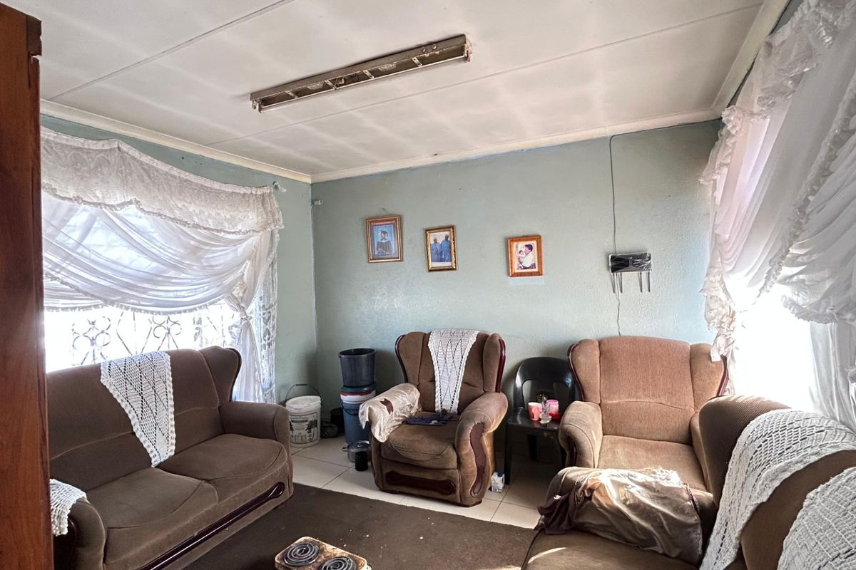 A living room featuring tiled flooring and security bars on the windows, currently showing signs of wear including ceiling damage and peeling paint.