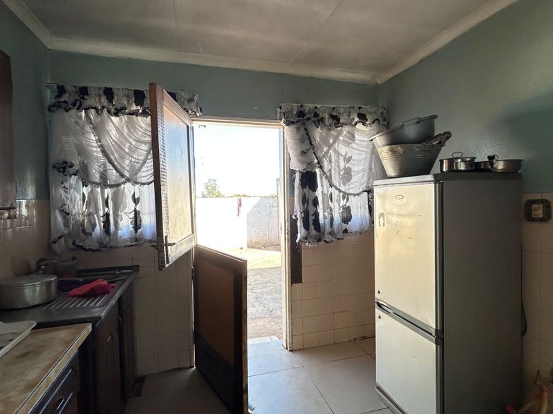 A functional kitchen featuring tiled splashbacks, built-in cabinetry, and direct access to the exterior, offering potential for modernization and cosmetic updates.