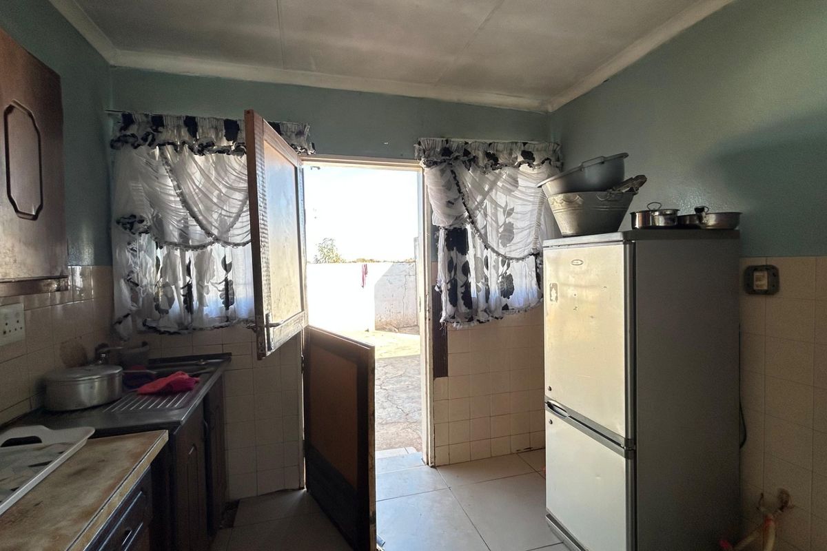 A functional kitchen featuring tiled splashbacks, built-in cabinetry, and direct access to the exterior, offering potential for modernization and cosmetic updates.