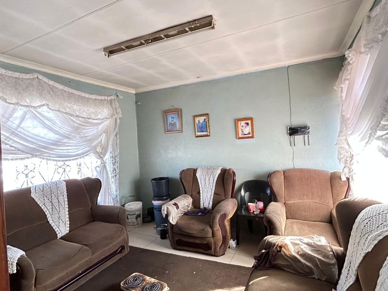 A living room featuring tiled flooring, security bars on windows, and a ceiling-mounted light fixture in need of maintenance.
