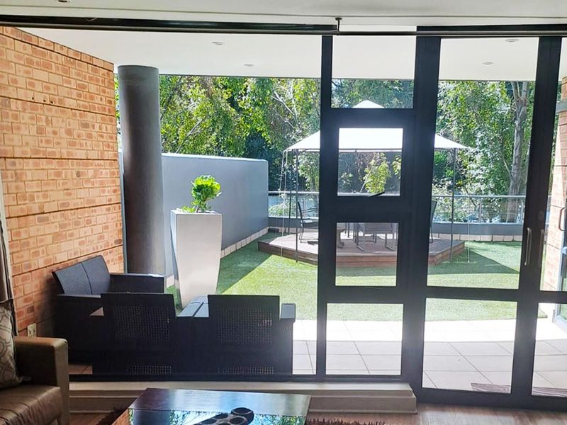 A covered patio area featuring exposed brick walls, tiled flooring, and large sliding glass doors that open onto a private garden space.