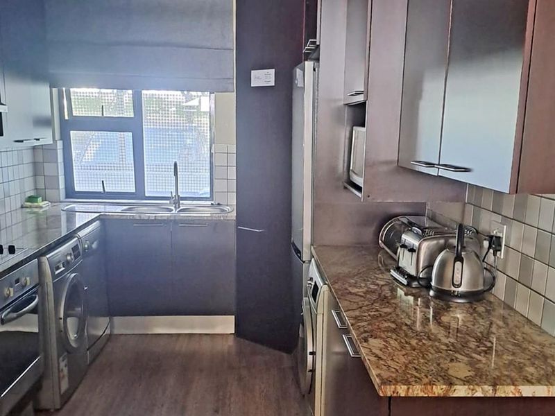 A functional kitchen featuring dark cabinetry, granite countertops, a double sink, and integrated appliances with a tiled backsplash and laminate flooring.