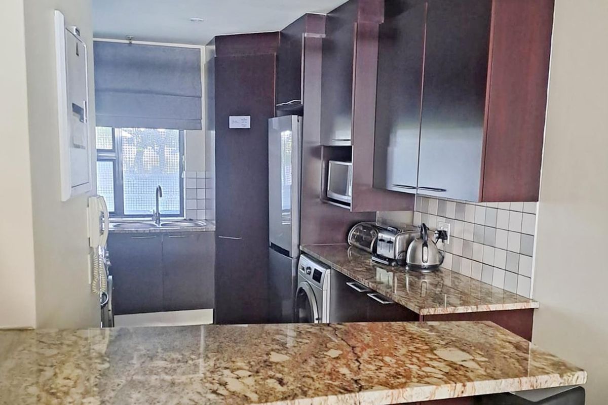 Compact kitchen featuring dark wood cabinetry, granite countertops, tiled backsplash, and integrated appliances, offering a functional and efficient workspace.