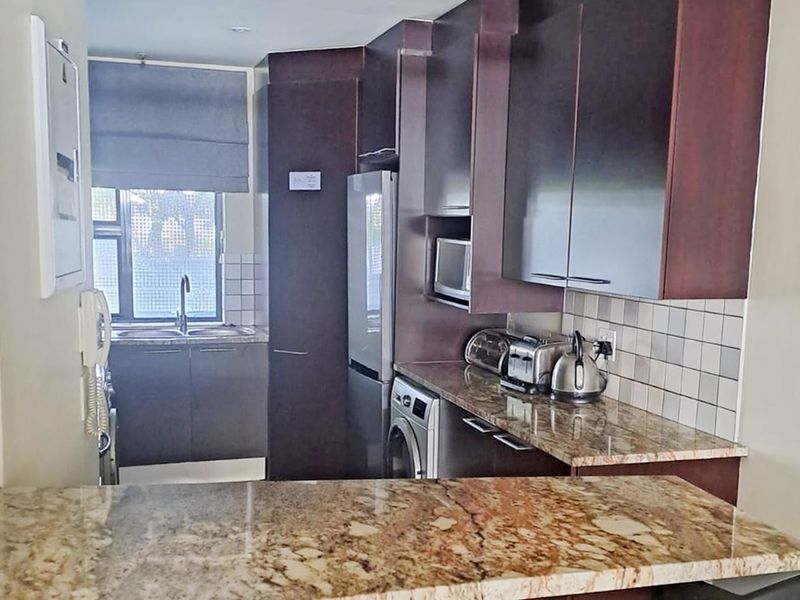 Compact kitchen featuring dark wood cabinetry, granite countertops, tiled backsplash, and integrated appliances, offering a functional and efficient workspace.