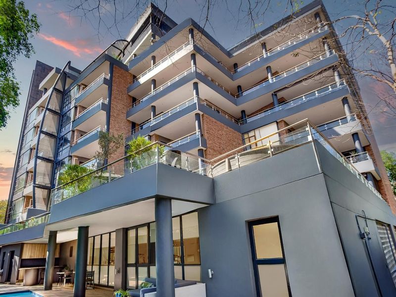 Modern multi-story apartment building featuring private balconies with glass balustrades, brick and rendered facade, and a ground-level swimming pool area.