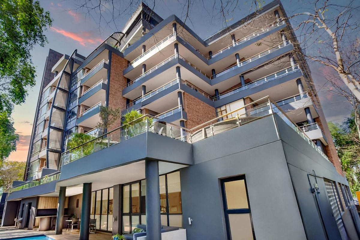 Modern multi-story apartment building featuring private balconies with glass balustrades, brick and rendered facade, and a ground-level swimming pool area.