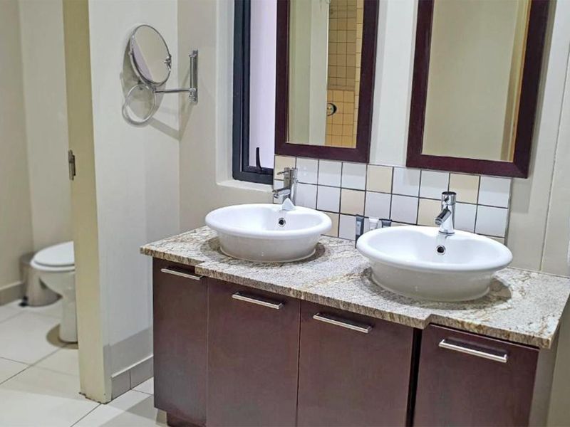 A well-maintained bathroom featuring a double vanity with granite countertops, vessel sinks, and a separate toilet area with tiled flooring.