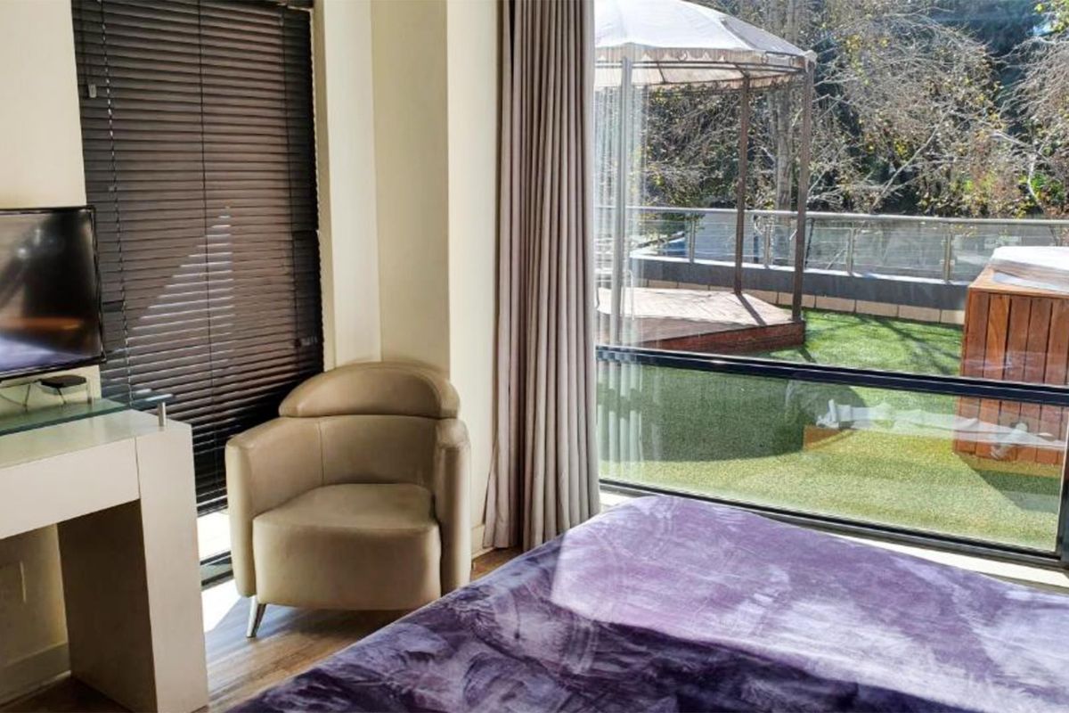 A bright bedroom featuring large floor-to-ceiling windows with direct access to an outdoor patio area.