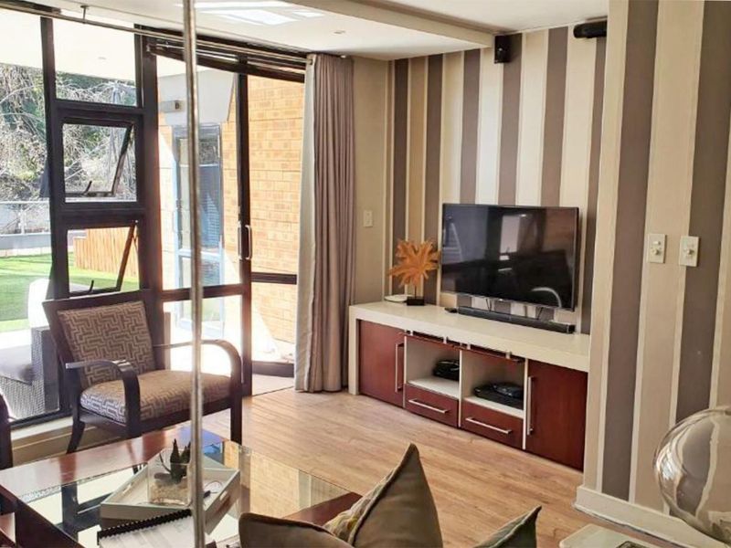 A bright living room featuring laminate flooring, striped wallpaper, and large glass sliding doors providing direct access to an outdoor patio area.