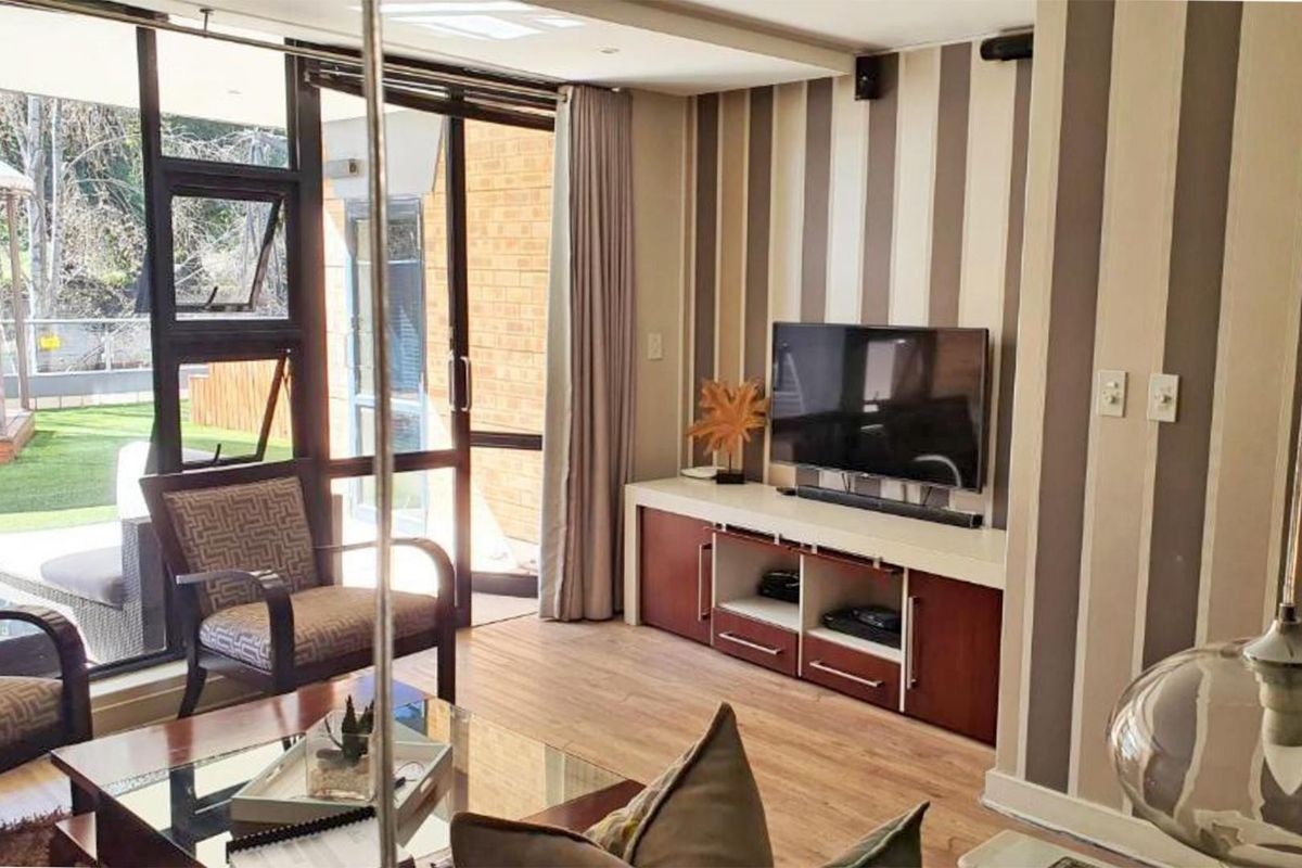 A bright living room featuring laminate flooring, striped wallpaper, and large glass sliding doors providing direct access to an outdoor patio area.