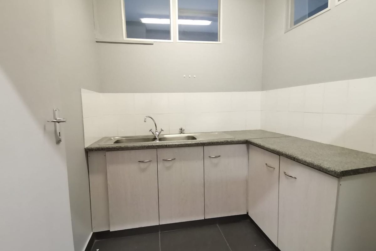 A functional kitchenette featuring light-toned cabinetry, granite countertops, a stainless steel double sink, and tiled finishes, suitable for office utility use.