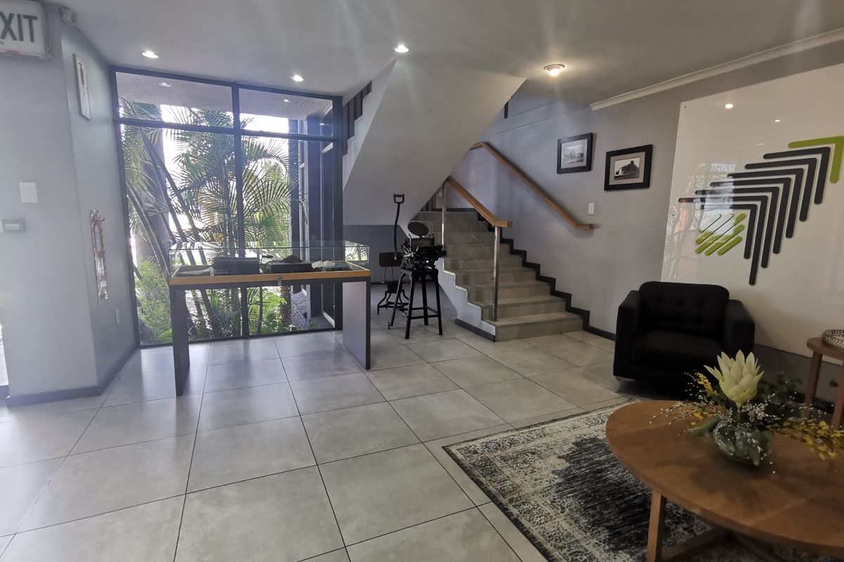 A bright and modern office entrance featuring tiled flooring, a prominent staircase with a handrail, and large windows providing natural light.