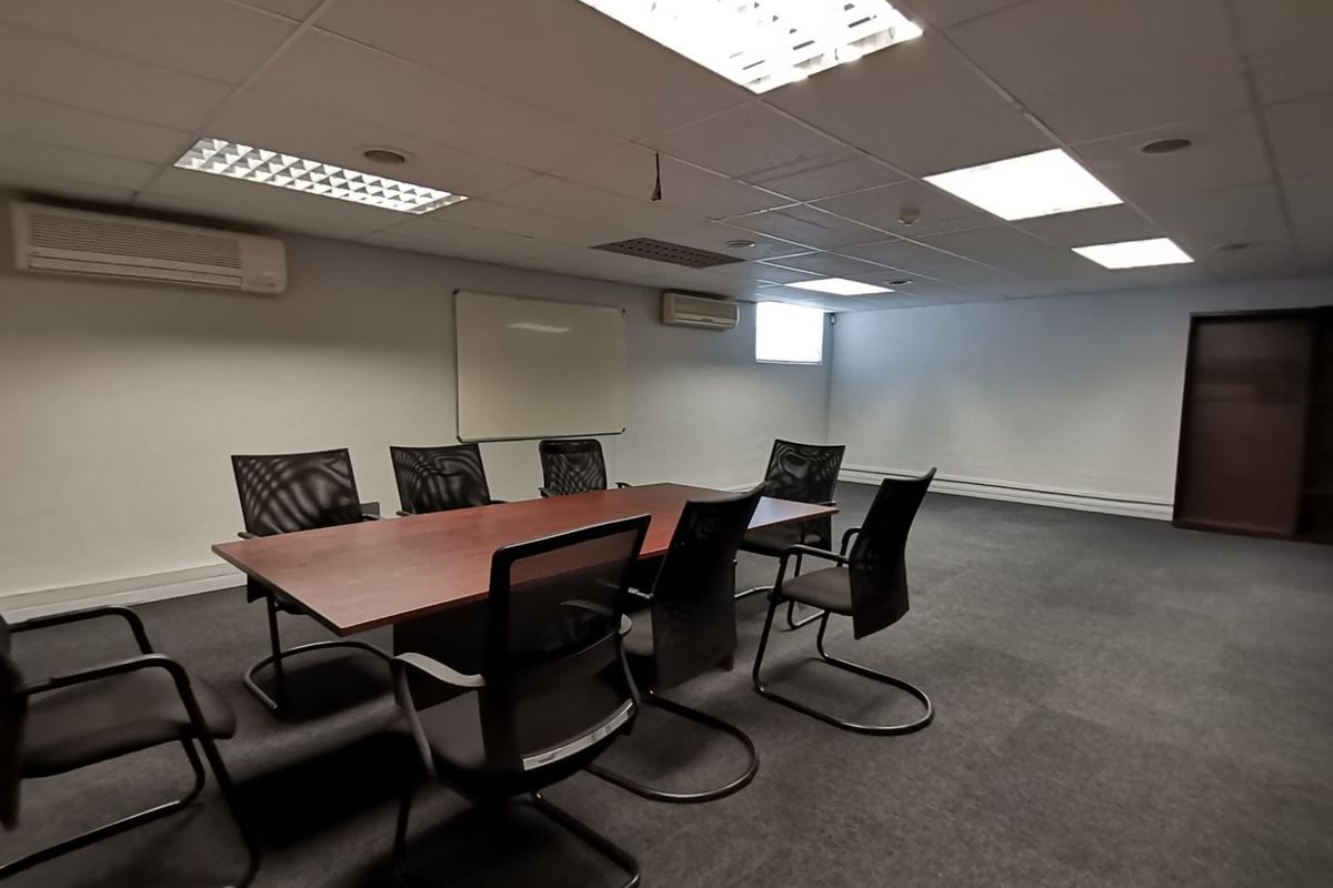 A functional office meeting room featuring a suspended ceiling, recessed lighting, wall-mounted air conditioning units, and carpeted flooring.