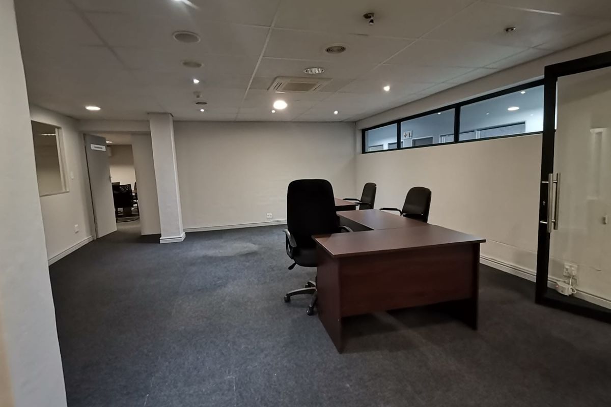 A functional office space featuring a suspended ceiling, recessed lighting, carpeted flooring, and a glass partition wall, providing a professional work environment.