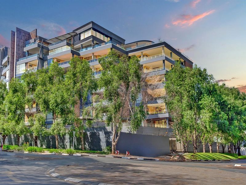 A modern multi-story apartment building featuring contemporary architecture, private balconies with glass balustrades, and well-maintained perimeter landscaping.
