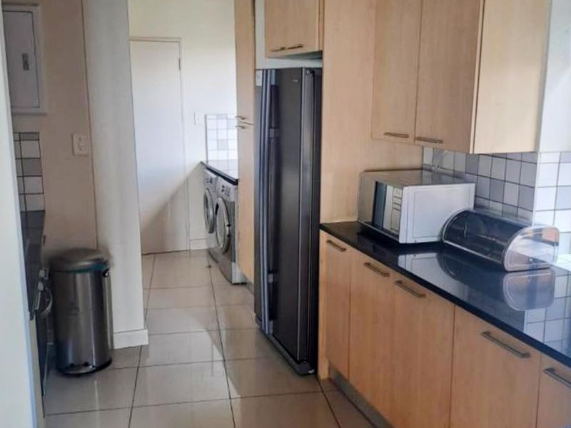 A functional kitchen featuring light wood cabinetry, dark granite countertops, tiled backsplash, and an adjacent laundry area with tiled flooring.