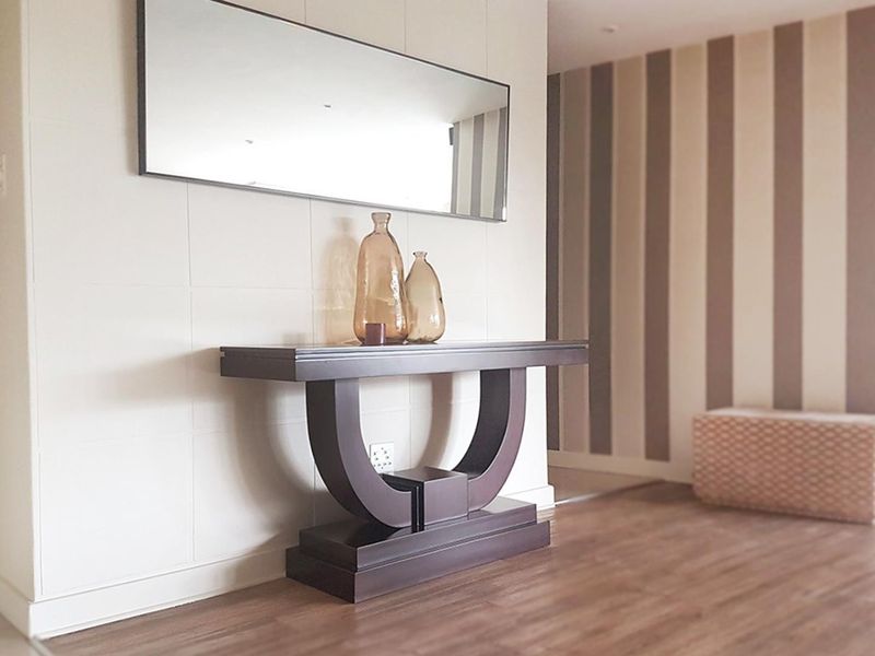 A welcoming entrance area featuring wood-look laminate flooring, a decorative striped feature wall, and a large wall-mounted mirror.