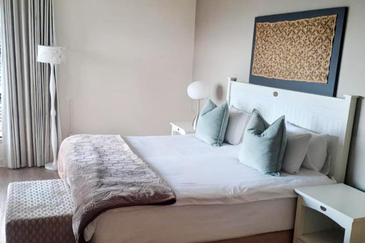 A well-maintained bedroom featuring neutral wall tones, laminate flooring, and floor-to-ceiling curtains.
