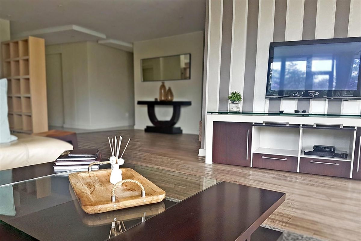 Spacious living area featuring modern laminate flooring, a decorative striped feature wall, and recessed ceiling lighting.