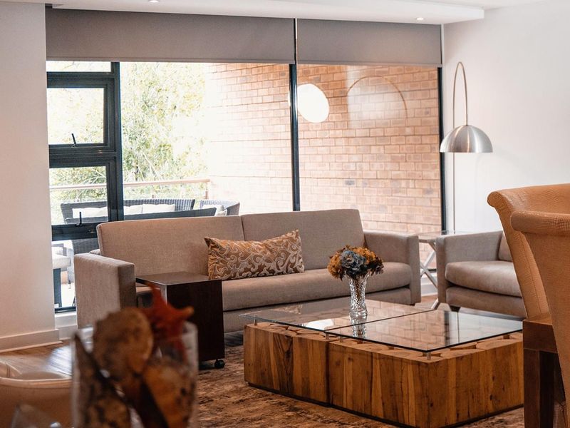 A bright and modern living room featuring large floor-to-ceiling windows, recessed lighting, and an attractive exposed brick feature wall.