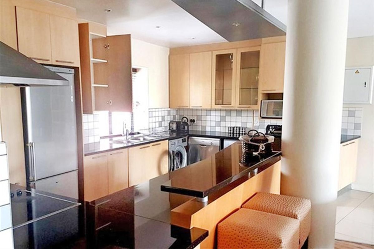 A functional kitchen featuring light wood cabinetry, dark granite countertops, a breakfast bar, and integrated appliances with a modern open-plan layout.