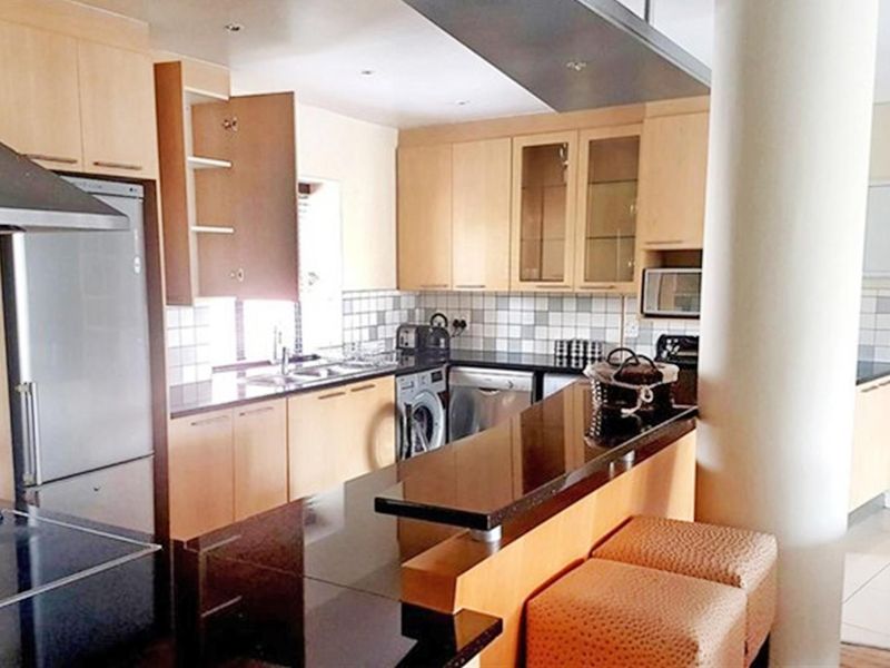 A functional kitchen featuring light wood cabinetry, dark granite countertops, a breakfast bar, and integrated appliances with a modern open-plan layout.