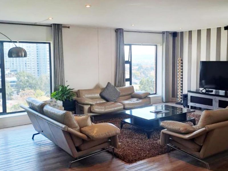 A spacious living room featuring large windows with city views, recessed downlighting, and modern laminate flooring.