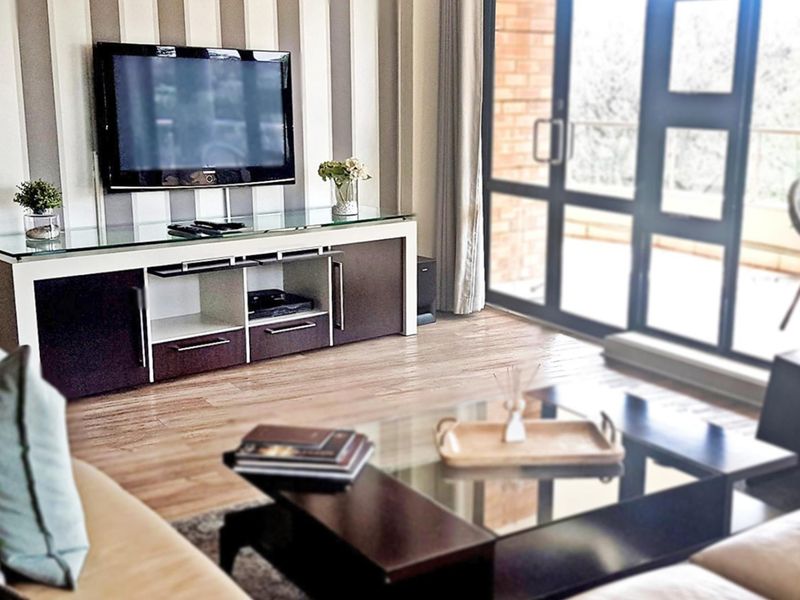 A well-lit living room featuring laminate flooring, striped wallpaper, and a large sliding glass door providing access to an outdoor area.