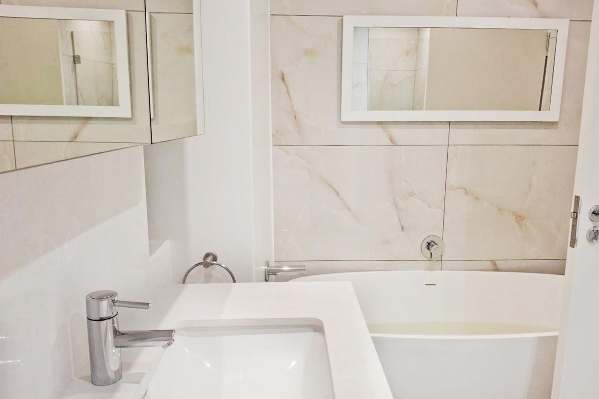 Modern bathroom featuring a sleek vanity basin with chrome mixer tap, built-in bathtub, and elegant marble-look wall tiling.