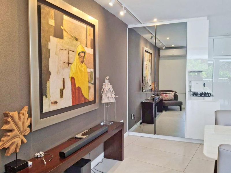 Modern open-plan living area featuring sleek tiled flooring, mirrored wall accents, and integrated track lighting, creating a bright and contemporary atmosphere.