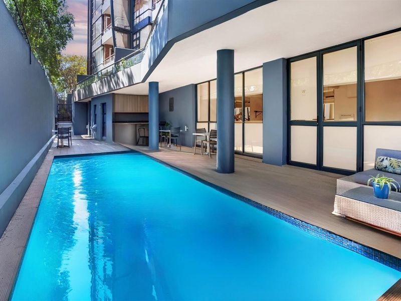 Modern apartment complex pool area featuring a sleek swimming pool, covered patio space, and built-in bar counter, perfect for outdoor relaxation and entertaining.