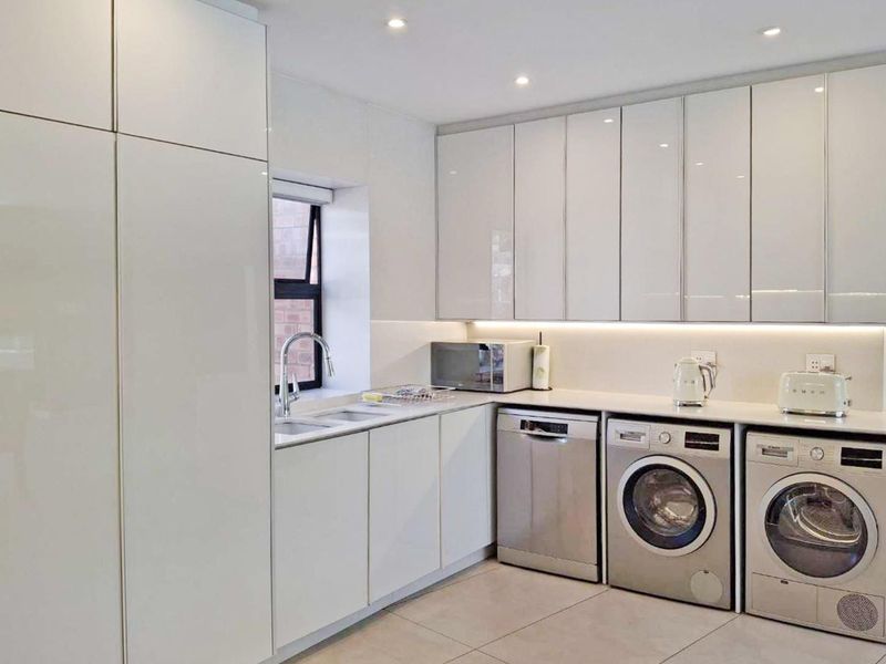 Modern kitchen featuring sleek high-gloss white cabinetry, integrated appliances, recessed lighting, and a clean, minimalist aesthetic with tiled flooring.