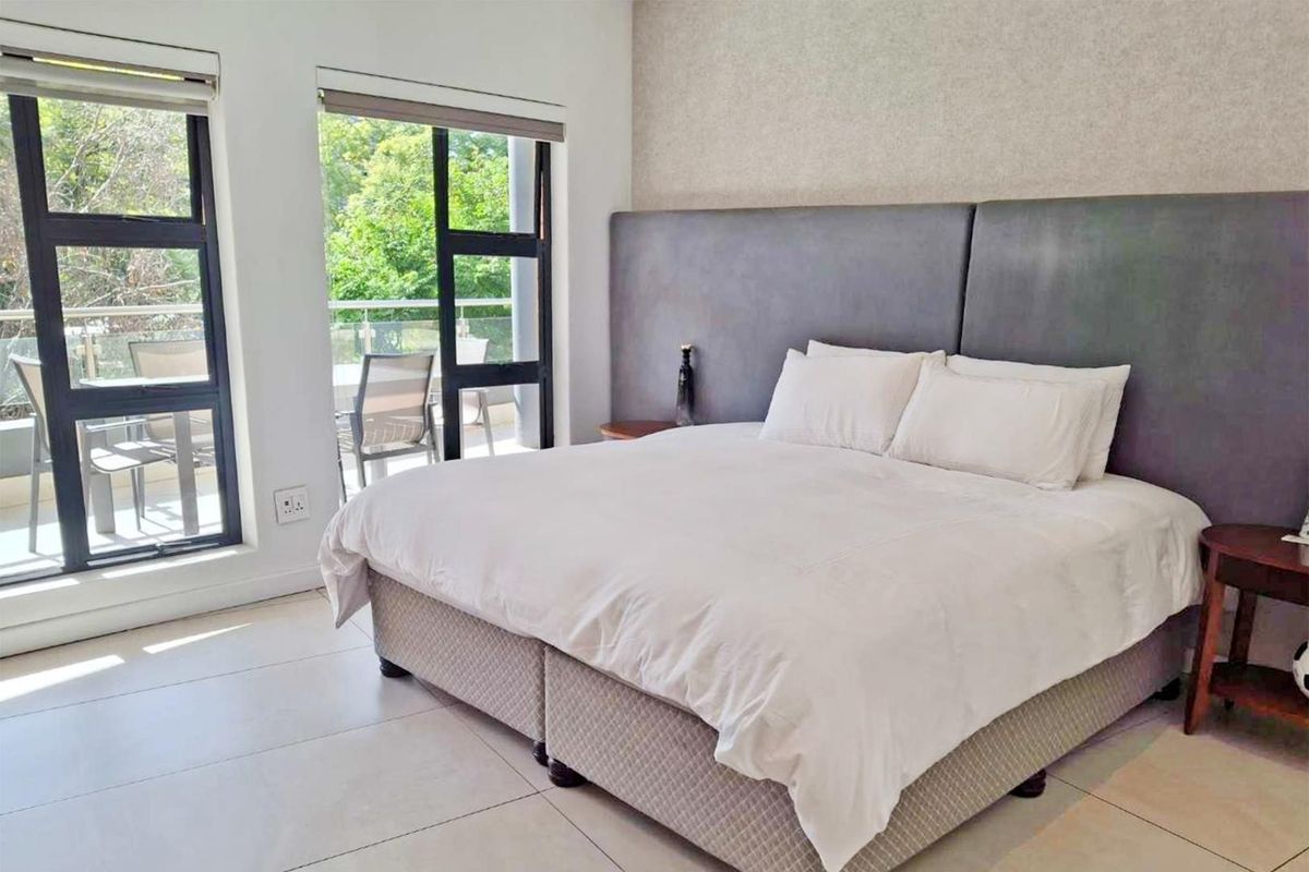 A bright and spacious bedroom featuring large windows, tiled flooring, and direct access to a private balcony.