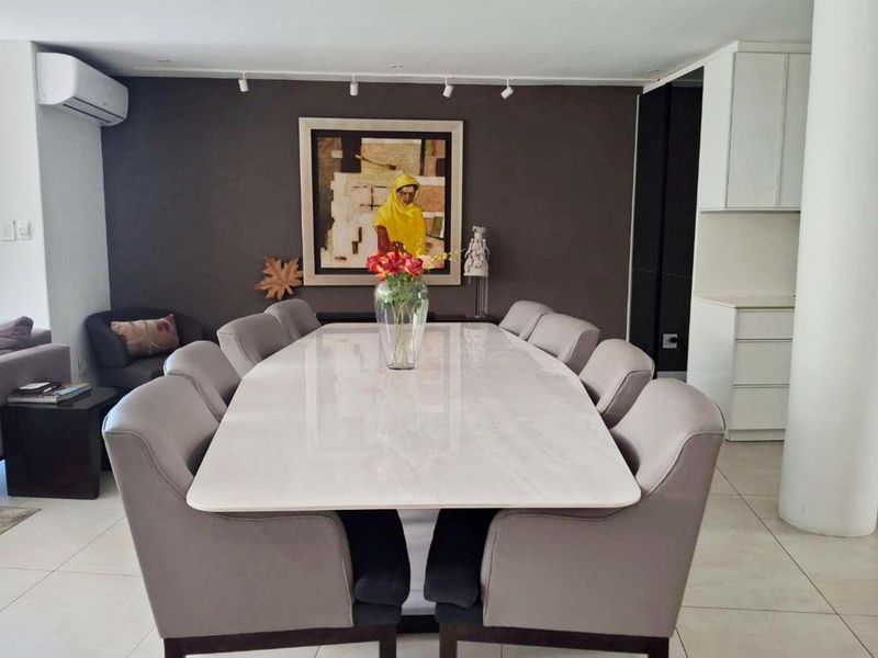 Spacious open-plan living and dining area featuring tiled flooring, modern track lighting, an integrated air conditioning unit, and a sleek built-in kitchen section.